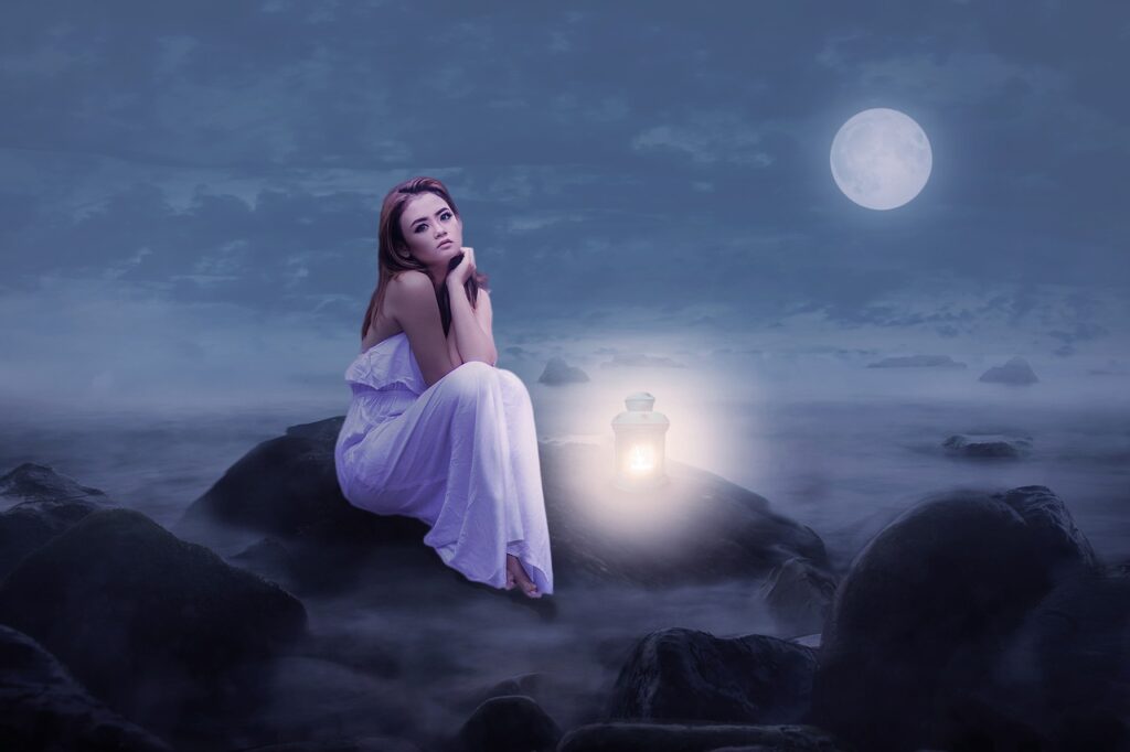 Woman sitting on a large rock on the beach on a full moon night.